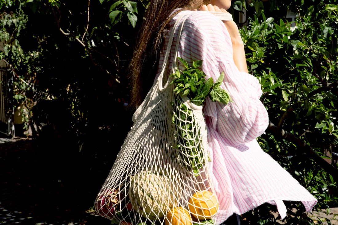 Eine junge Frau trägt ihre frischen Einkäufe in einem klassischen Einkaufsnetz.