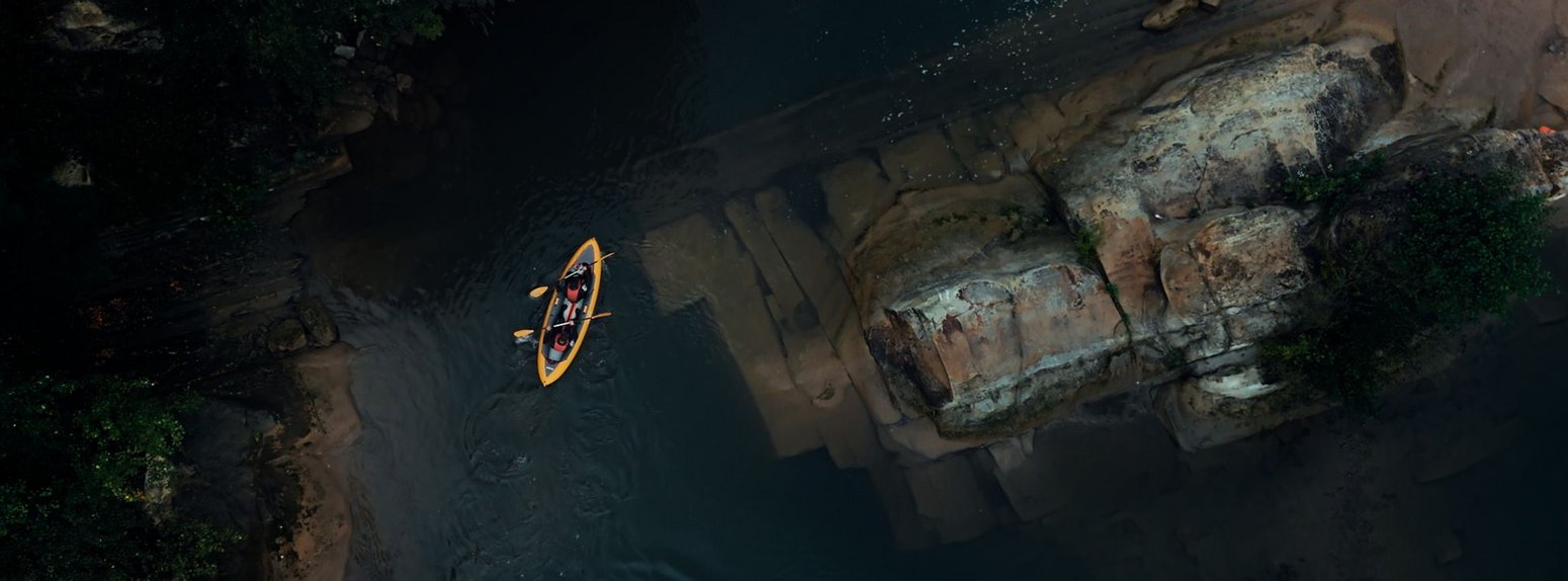 Zwei Kanufahrer aus der Vogelperspektive auf einem ruhigen Fluss.