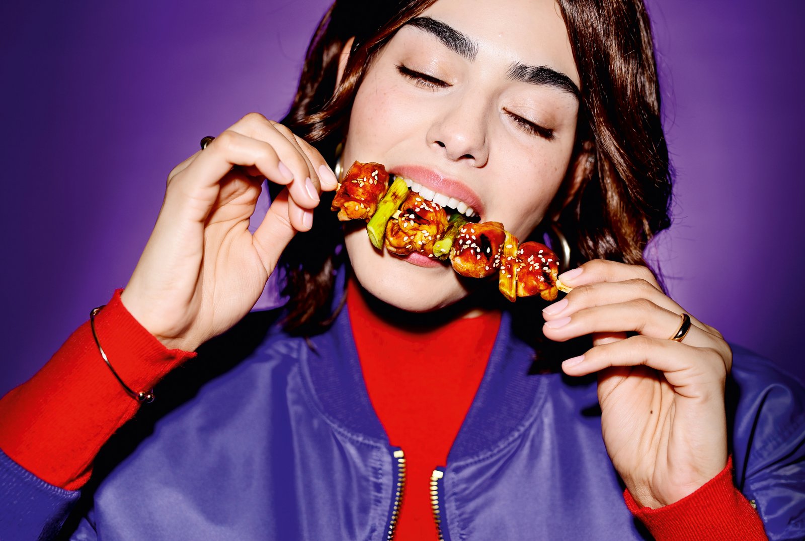 Closeup einer jungen Frau, die genüsslich in einen asiatischen Hähnchenspieß beißt.