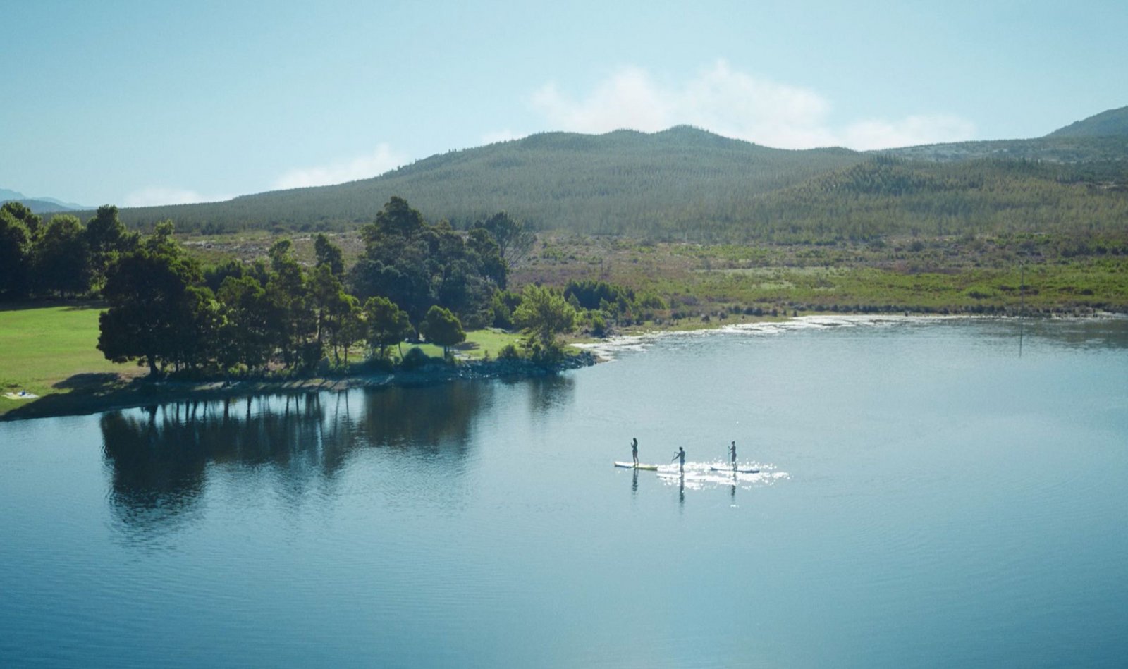 Weitwinkliger Blick auf einen sommerlichen See, Menschen auf Stand-up-Paddleboards.