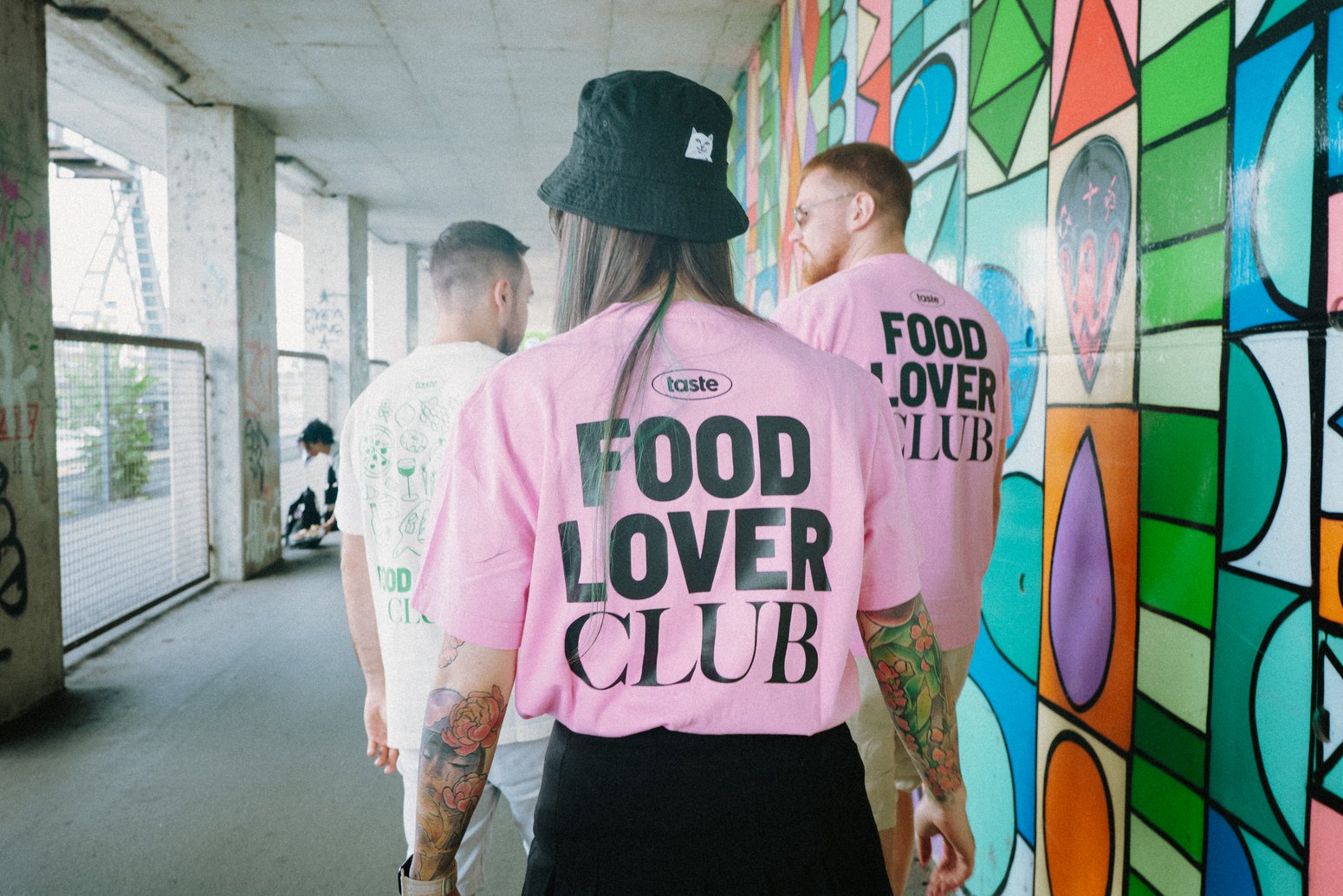 Junge Menschen mit Merch-Artikeln des Food Lover Clubs, T-Shirts, moderne Shopping Bags, dazwischen illustrative Salz- und Pfefferstreuer.